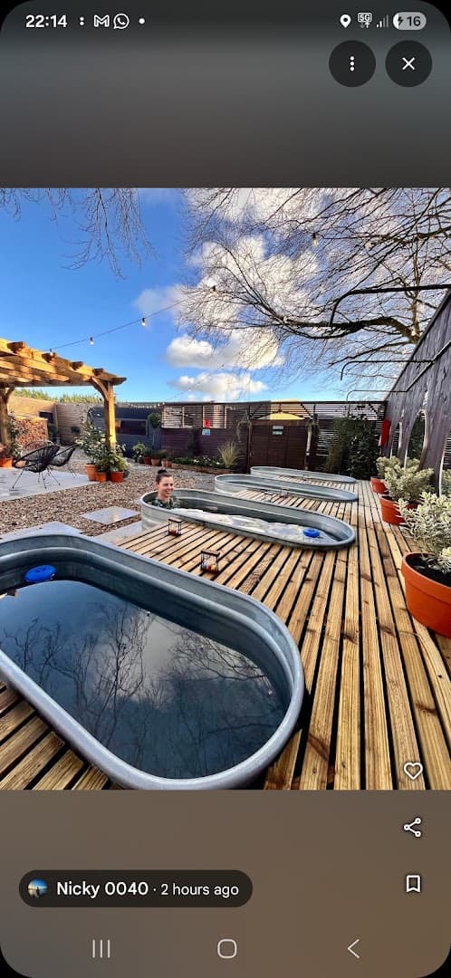Several metal stock tanks filled with water are arranged on a wooden deck in an outdoor setting under a blue sky.