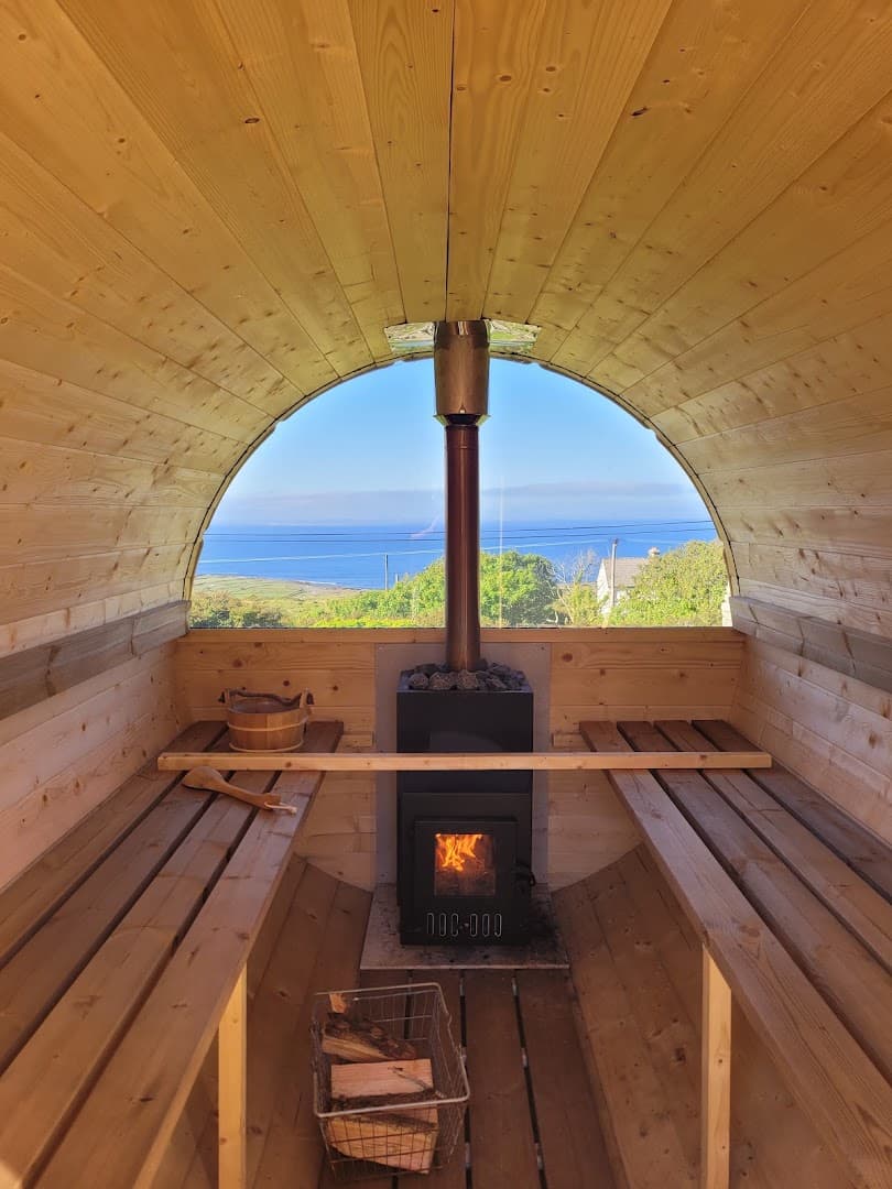 Inside a wooden barrel sauna looking out a window at the sea.