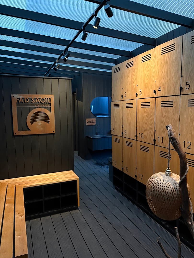 Interior view of a sauna with wooden lockers, benches, and a sign reading "FAD SAOIL SAUNAS.