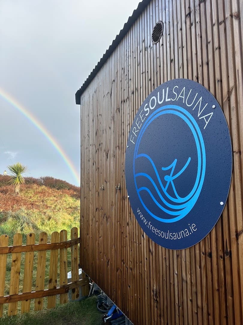 Side view of a wooden sauna structure with a circular sign and a rainbow in the sky.