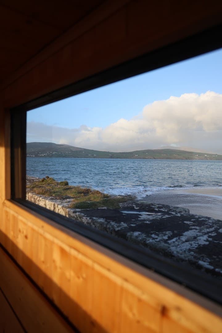 View of the sea and green hills through the window of a wooden sauna in Ireland.