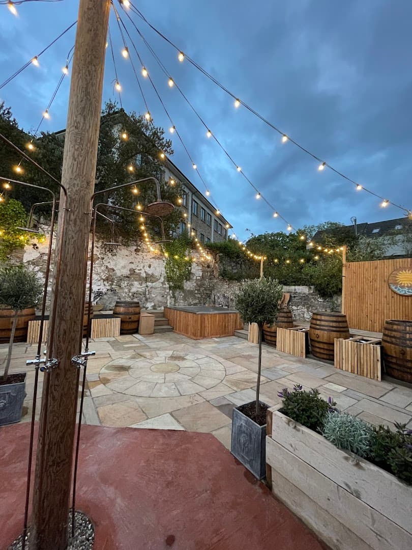 An outdoor sauna and stone patio area are illuminated by string lights against a dusky sky.