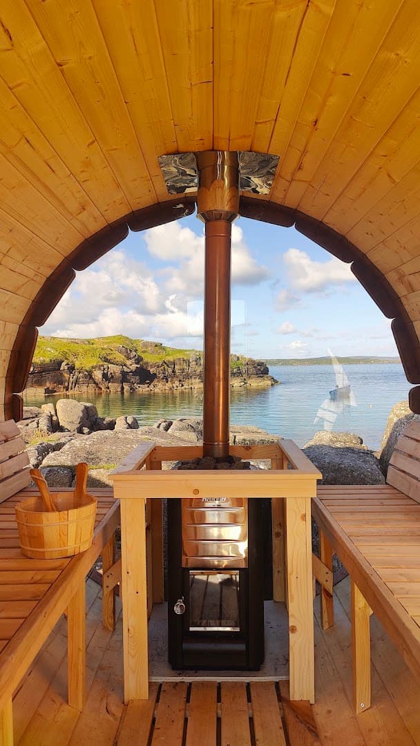 Interior of a wooden barrel sauna looking out at a rocky coastline and the sea.