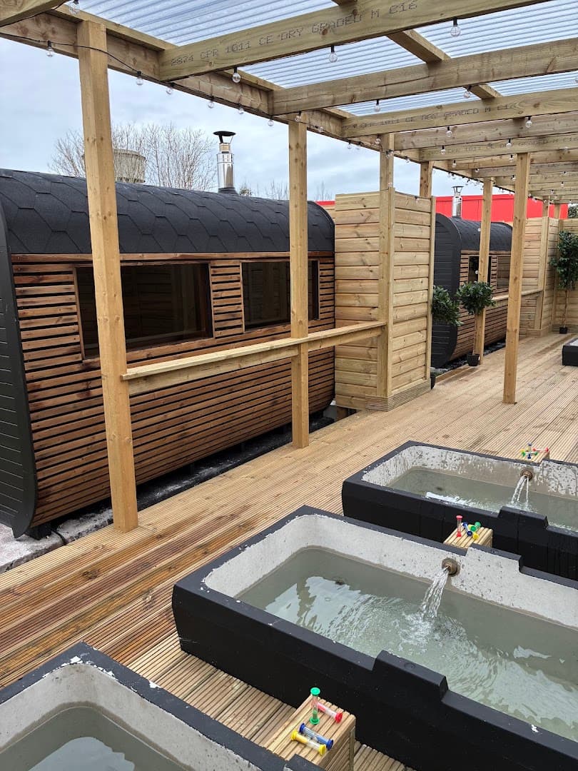 Wooden saunas and ice baths sit on an outdoor deck with a pergola above.
