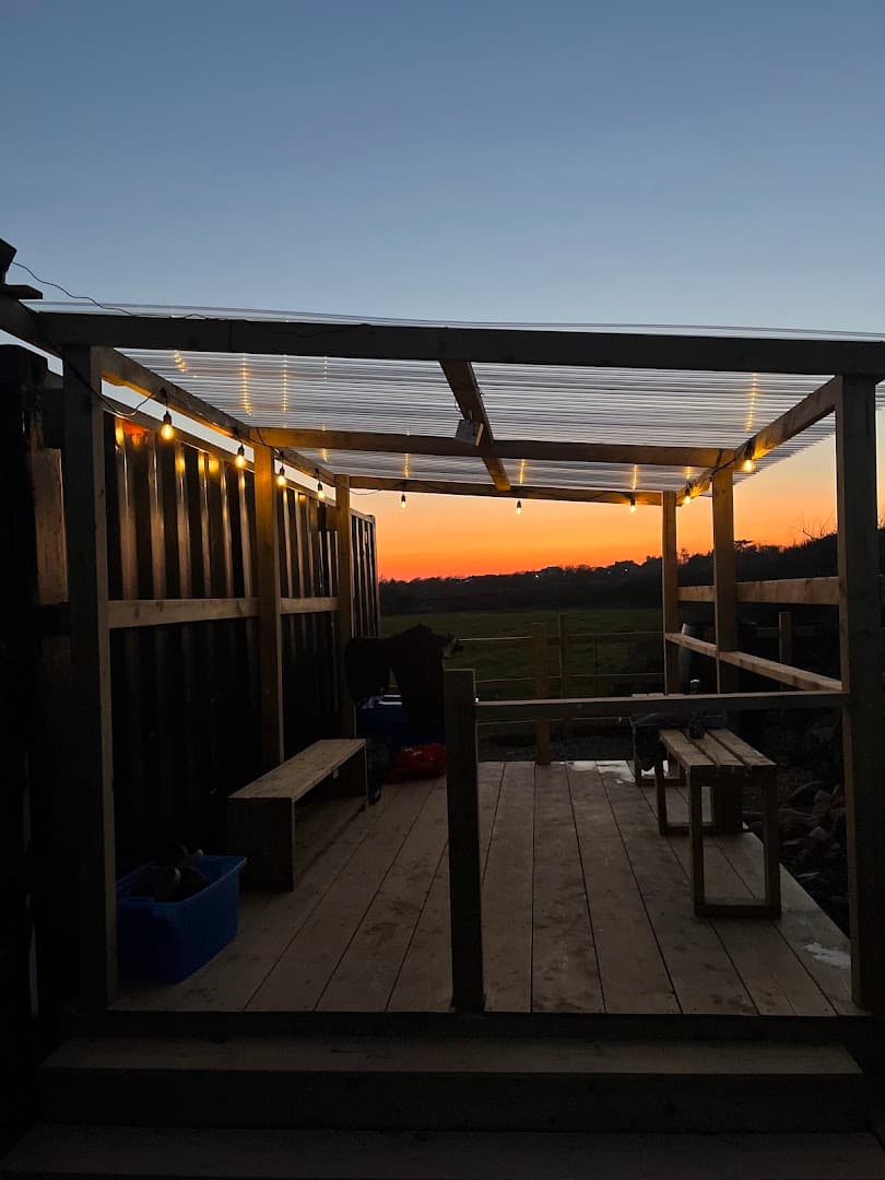 A wooden outdoor structure with benches overlooks a field at sunset.