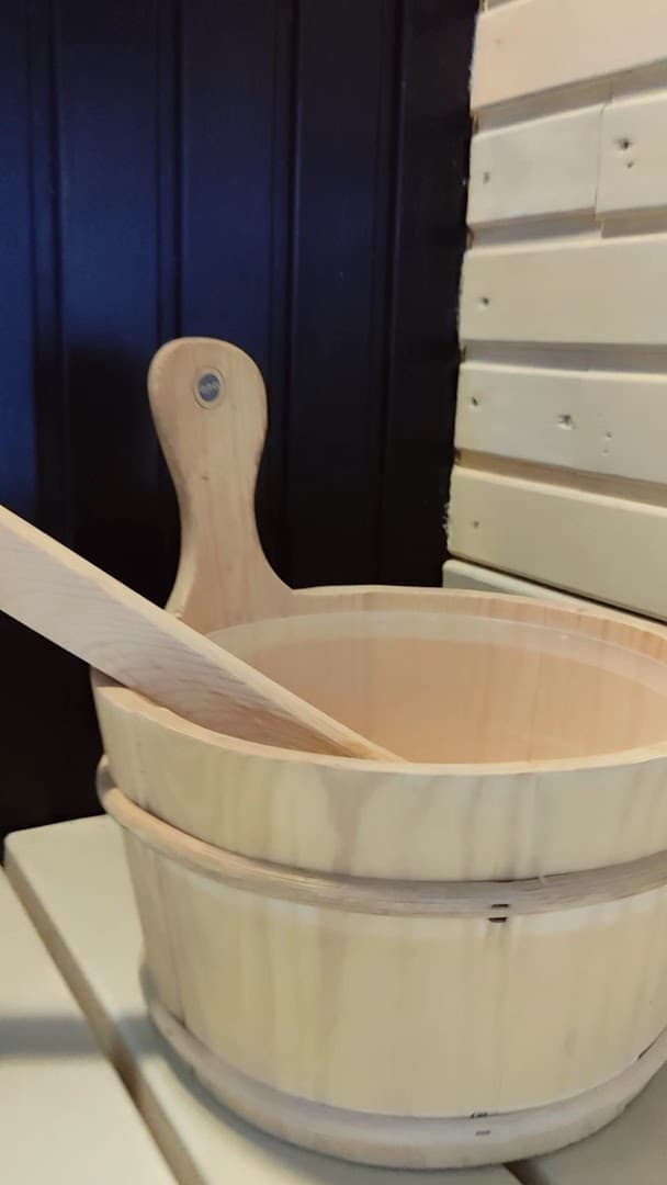 A wooden sauna bucket and ladle sit on a bench inside a sauna.