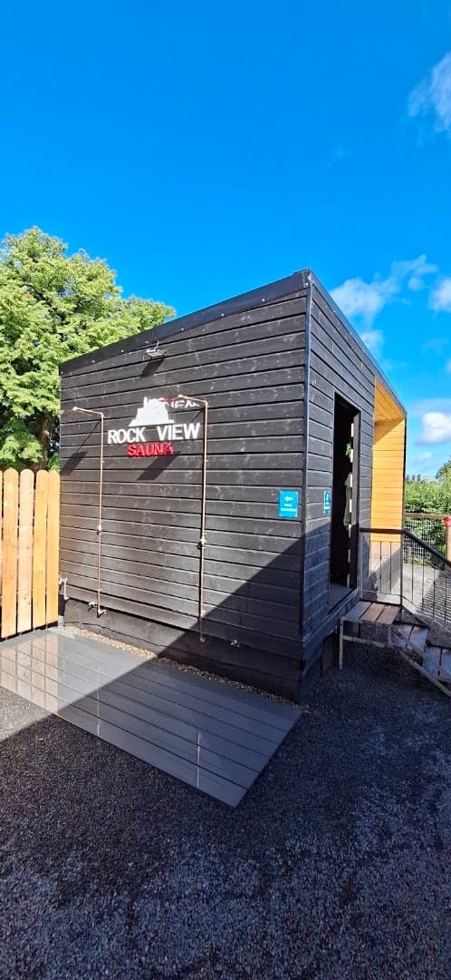 Exterior view of the dark wood Rock View Sauna structure under a bright blue sky.