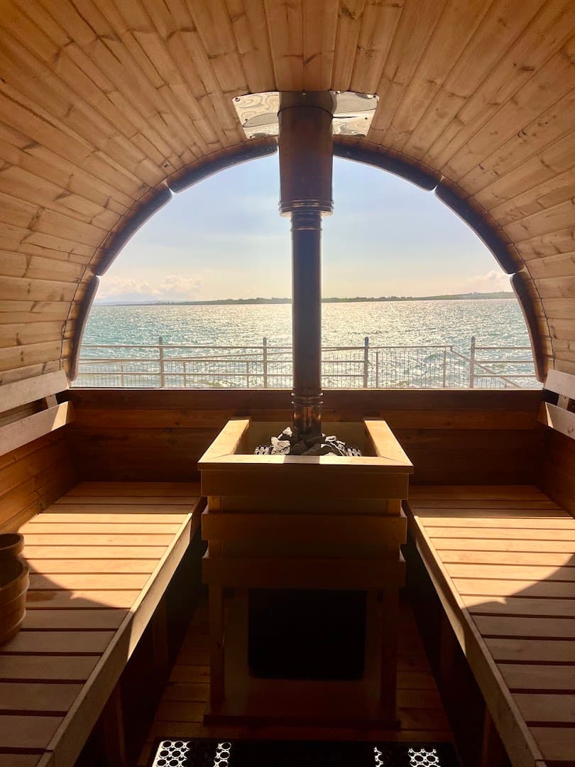 Interior of the wooden barrel sauna showing the benches and stove facing a window with a sea view.