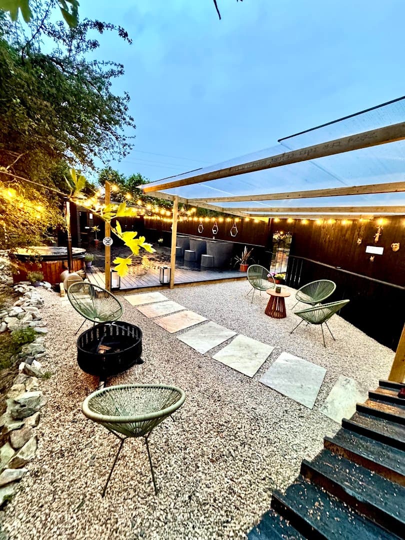 An outdoor wellness area features a hot tub, a pergola, and several lounge chairs arranged on a gravel patio.