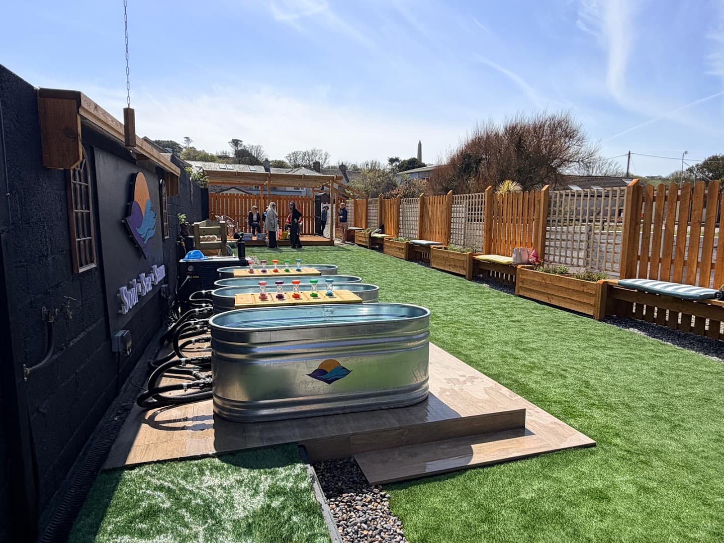 Outdoor area of Soul Sea Sauna in Ardmore with metal tubs on wooden platforms and artificial grass.