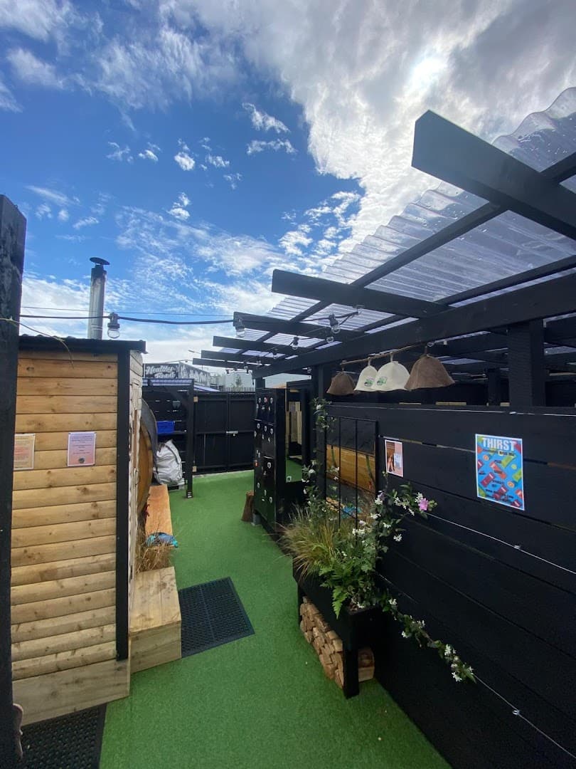 Outdoor area with a wooden barrel sauna structure, green turf flooring, and a covered patio with black walls.