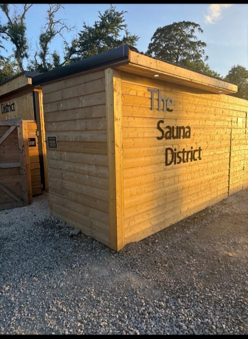 Exterior of "The Sauna District" wooden building in Ireland, with gravel ground and trees in the background.