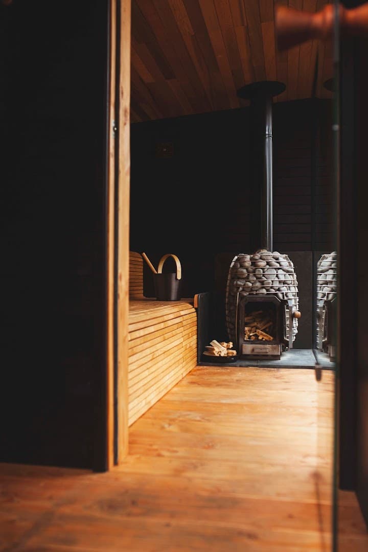 Interior view of a modern wooden sauna featuring a stone-filled wood-burning stove and wooden bench.