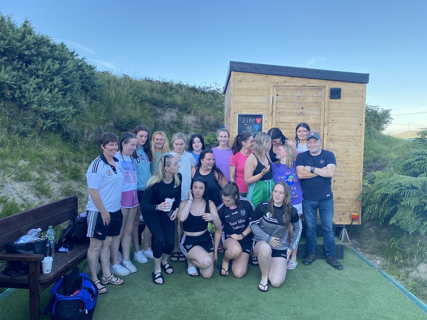 A group of people standing outside a wooden sauna structure outdoors.