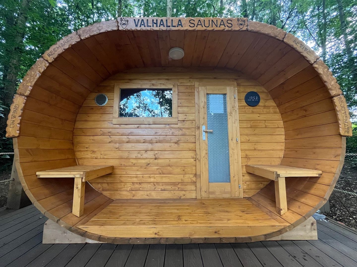 The wooden Valhalla Saunas barrel structure sits on a deck surrounded by trees.
