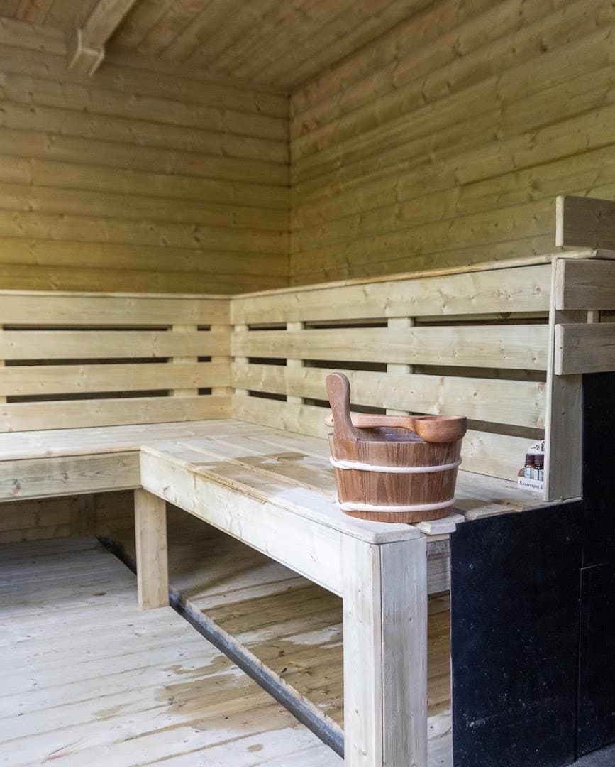 Interior of a wooden sauna featuring slatted benches, a bucket, and a ladle.