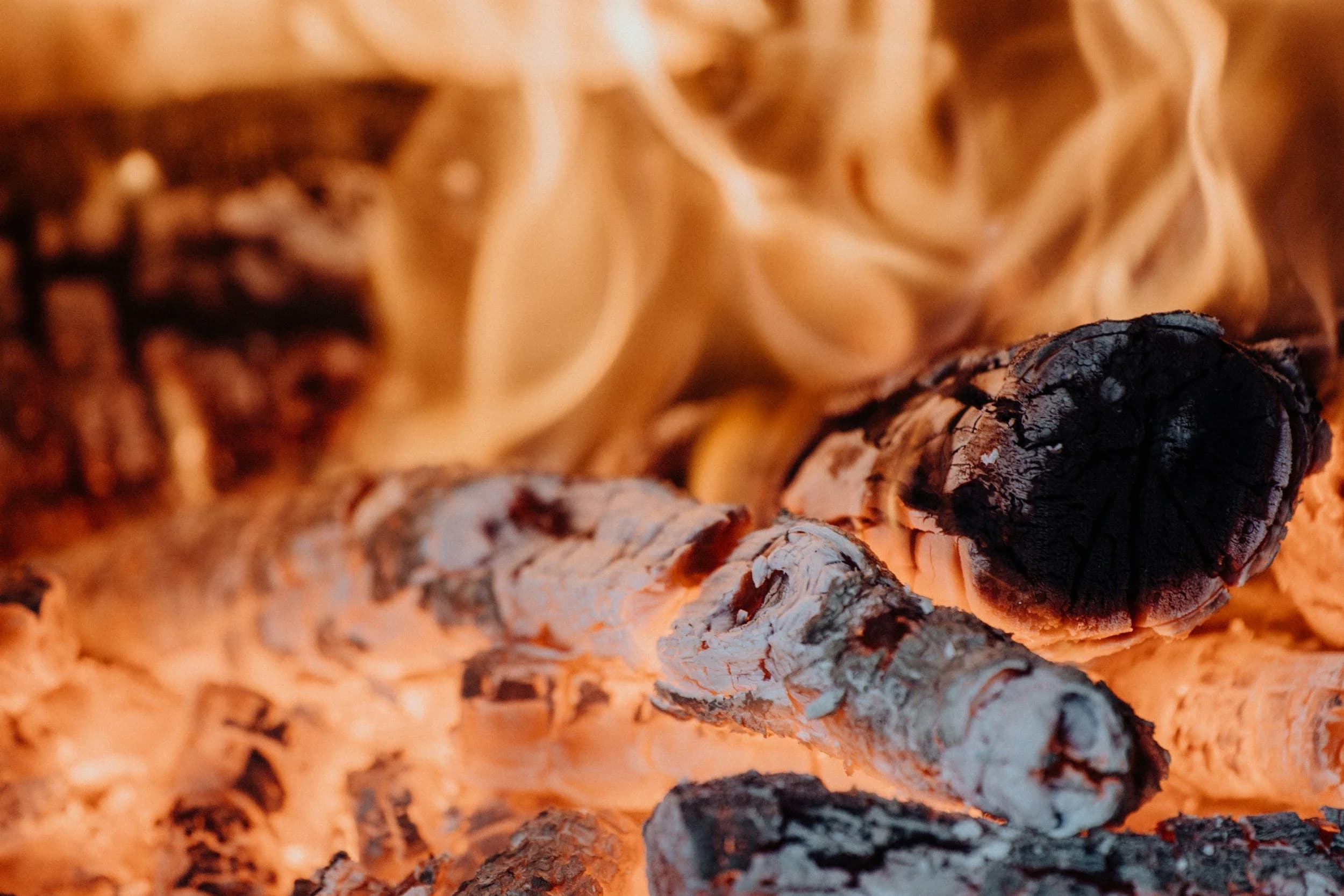 Close-up of burning logs with glowing embers and flames in a fireplace.